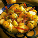 Rustic potato skillet with golden-brown potatoes, crispy bacon, and cabbage, sprinkled with fresh parsley.