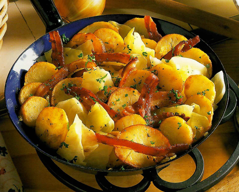 Rustic potato skillet with golden-brown potatoes, crispy bacon, and cabbage, sprinkled with fresh parsley.