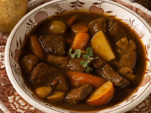Traditional German beef stew served in a rustic bowl with carrots, potatoes, and mushrooms in a rich red wine sauce.