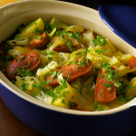 Hearty German sausage stew with cabbage, carrots, and potatoes in a blue casserole dish, topped with parsley.