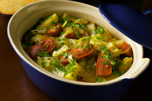 Hearty German sausage stew with cabbage, carrots, and potatoes in a blue casserole dish, topped with parsley.